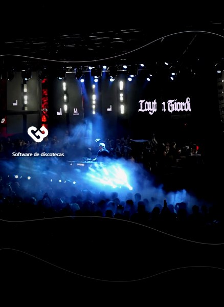 Vista aérea de un evento de música electrónica: escenario con pantallas, humo y luces azules sobre el público